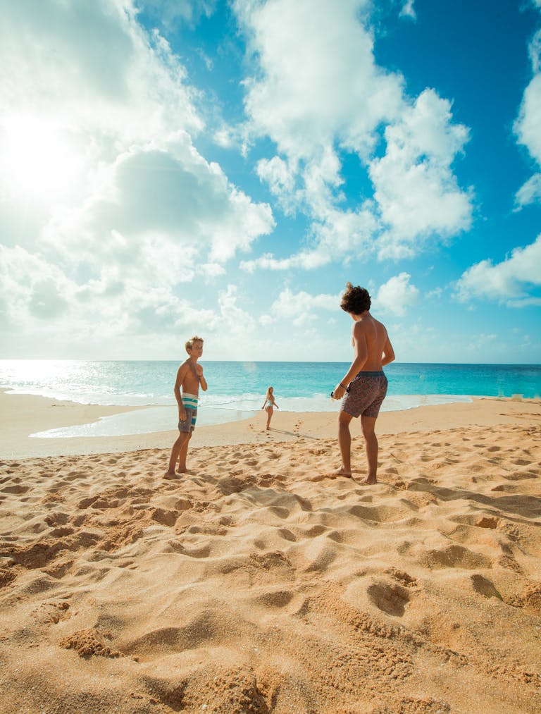Three children enjoy a sunny day playing on Waialua Beach, Hawaii, with clear skies and blue ocean waters.